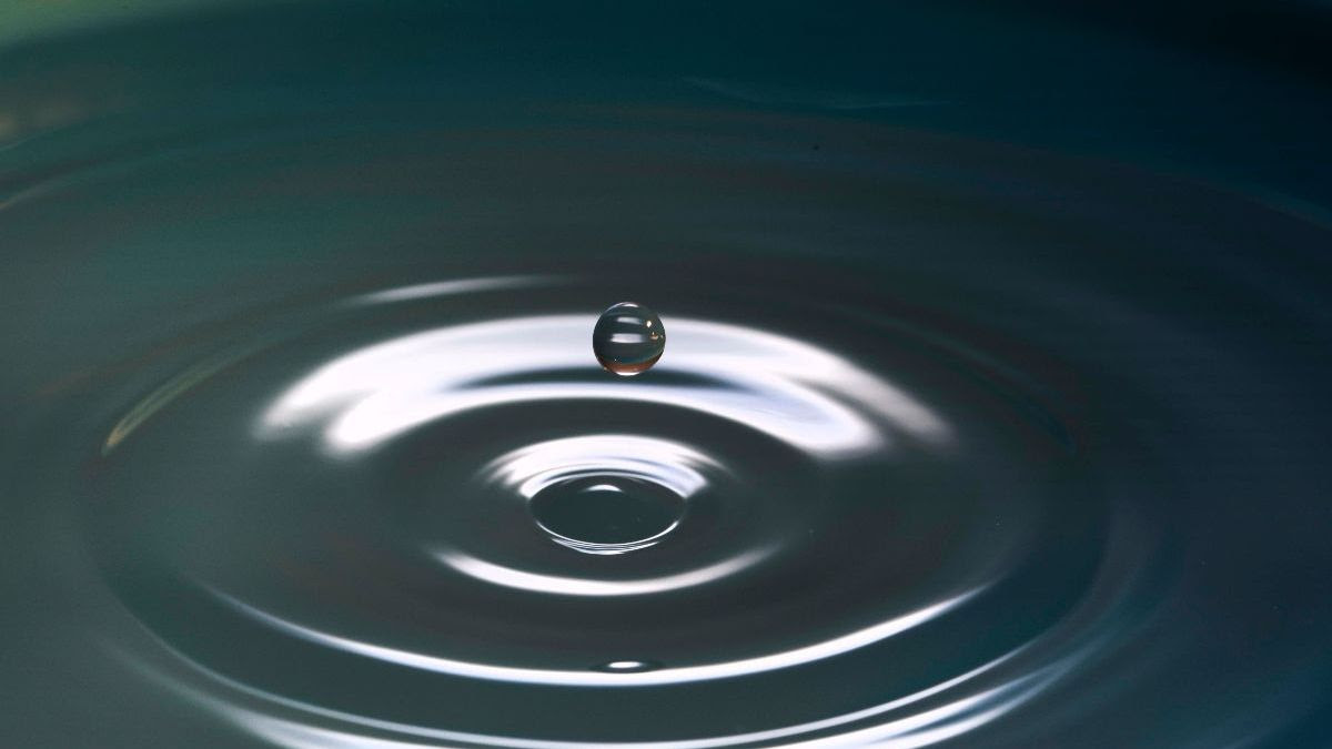 The image shows a drop of water suspended above a pool with concentric circles radiating out from a center point.